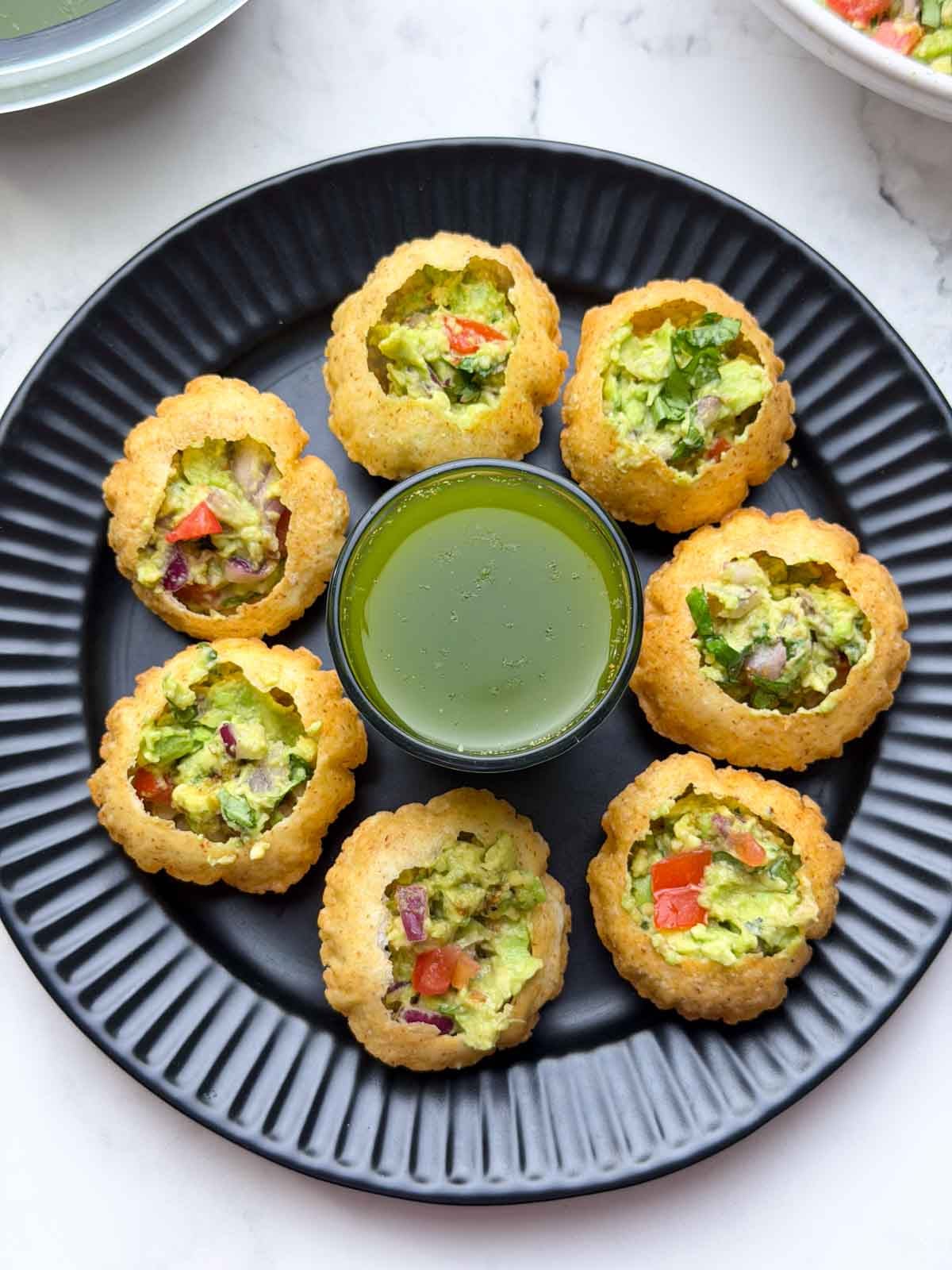 Mexican Golgappa filled with avocado stuffing arranged on a black plate.
