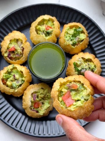 Mexican Golgappa filled with avocado stuffing and pani and avocado stuffing arranged on a plate and plain poori on the side.