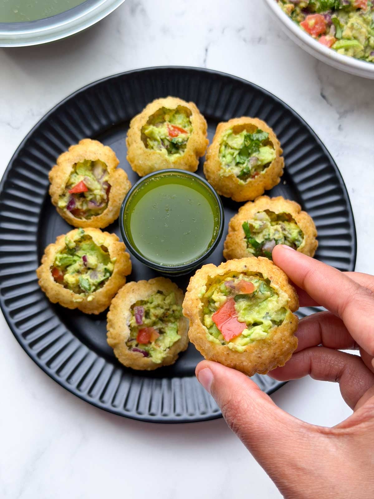 Mexican Golgappa filled with avocado stuffing and pani and avocado stuffing arranged on a plate and plain poori on the side.