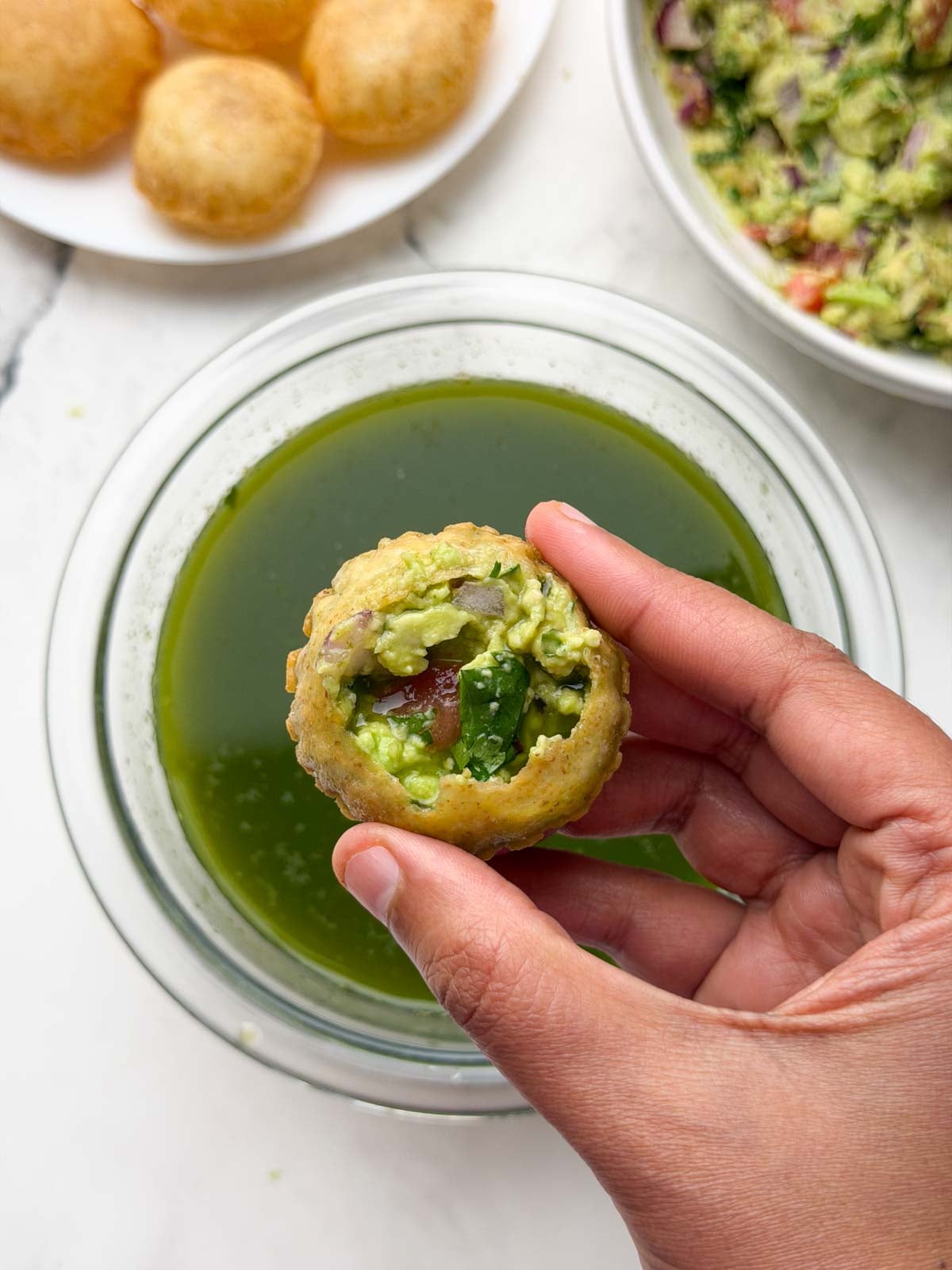 pani puri filled with avocado stuffing and pani with avocado stuffing and plain poori on the side.