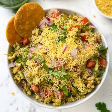 bhel puri chaat served in a white bowl garnished with sev and papdi on the side
