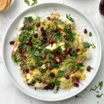 dahi papdi served in a white plate garnished with sev and papdi, dev and chutneys on the side