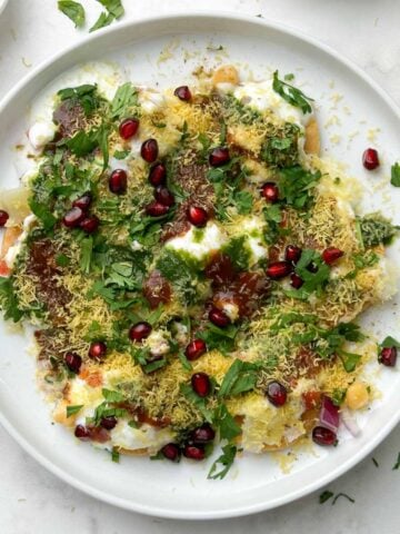 dahi papdi served in a white plate garnished with sev and papdi, dev and chutneys on the side