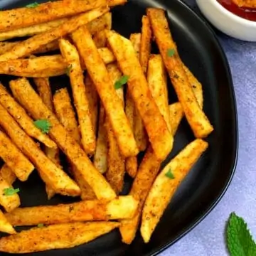 Crispy Masala French Fries served on a black plate with tomato ketchup