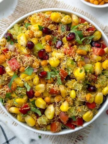 sweet corn bhel/corn chaat served in a bowl garnished with cilantro and pomegranate with boondi and sev on the side