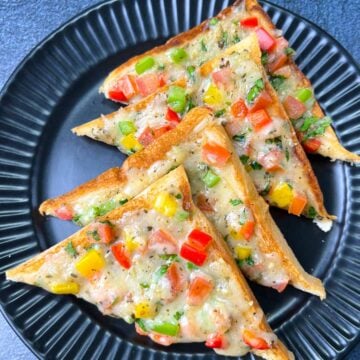 Veg chili cheese toast placed in a layer on a black plate