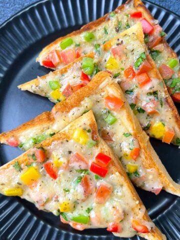 Veg chili cheese toast placed in a layer on a black plate