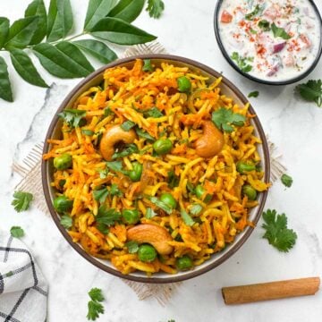 carrot rice served in a bowl with raita on the side along with spices and curry leaves