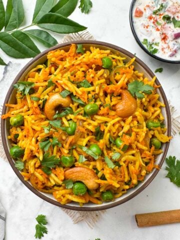 carrot rice served in a bowl with raita on the side along with spices and curry leaves