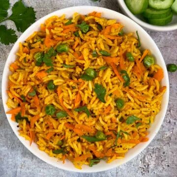 Carrot Rice served in a bowl garnished with coriander leaves and sliced cucumber on side