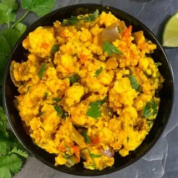 Dry Paneer Bhurji served in a black bowl with lemon wedge on side