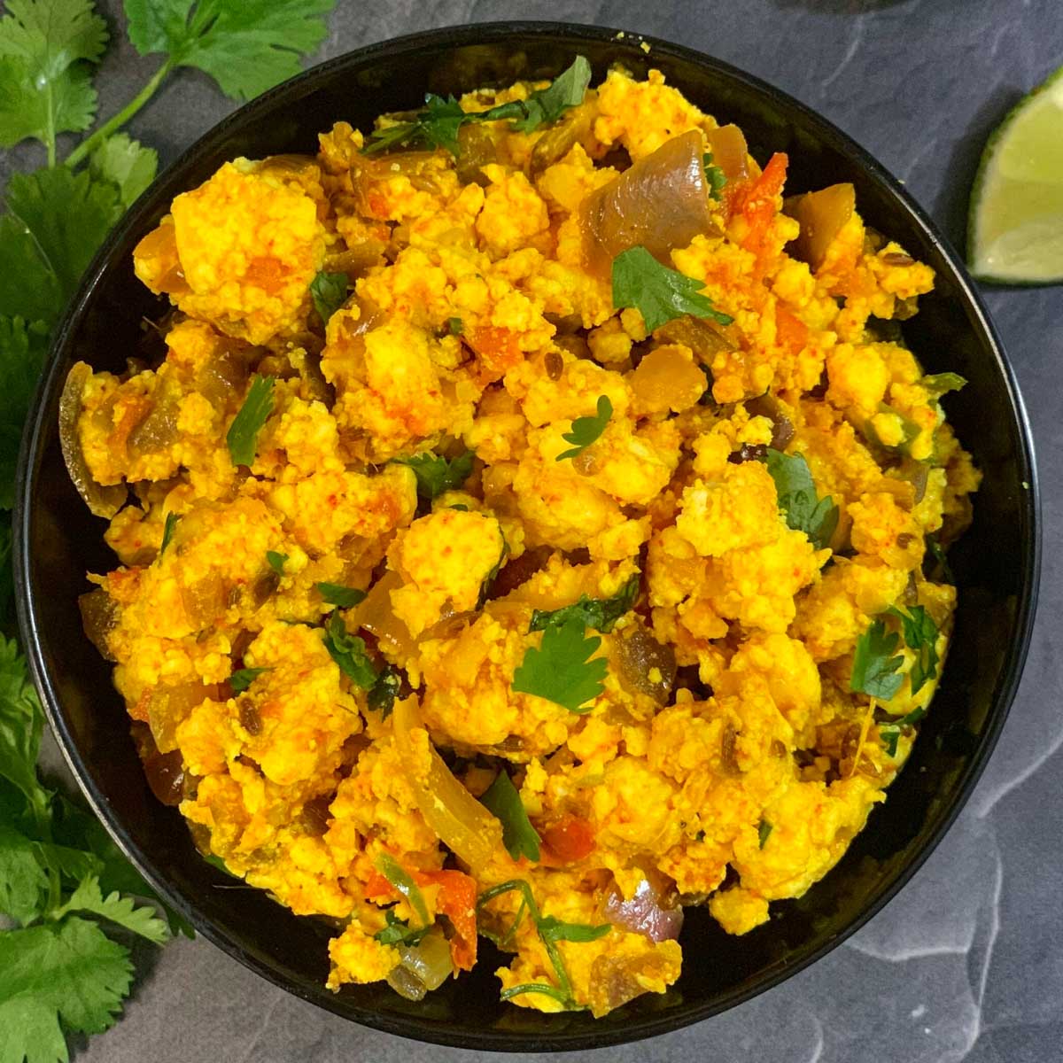 Dry Paneer Bhurji served in a black bowl with lemon wedge on side