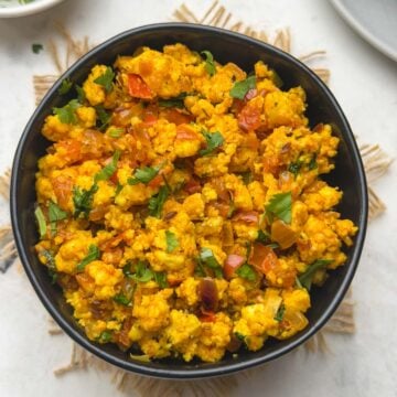 Paneer bhurji served in a black bowl with white bread and coriander leaves for garnish served on the side.