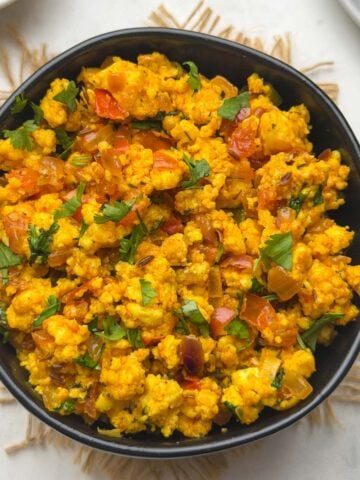 Paneer bhurji served in a black bowl with white bread and coriander leaves for garnish served on the side.