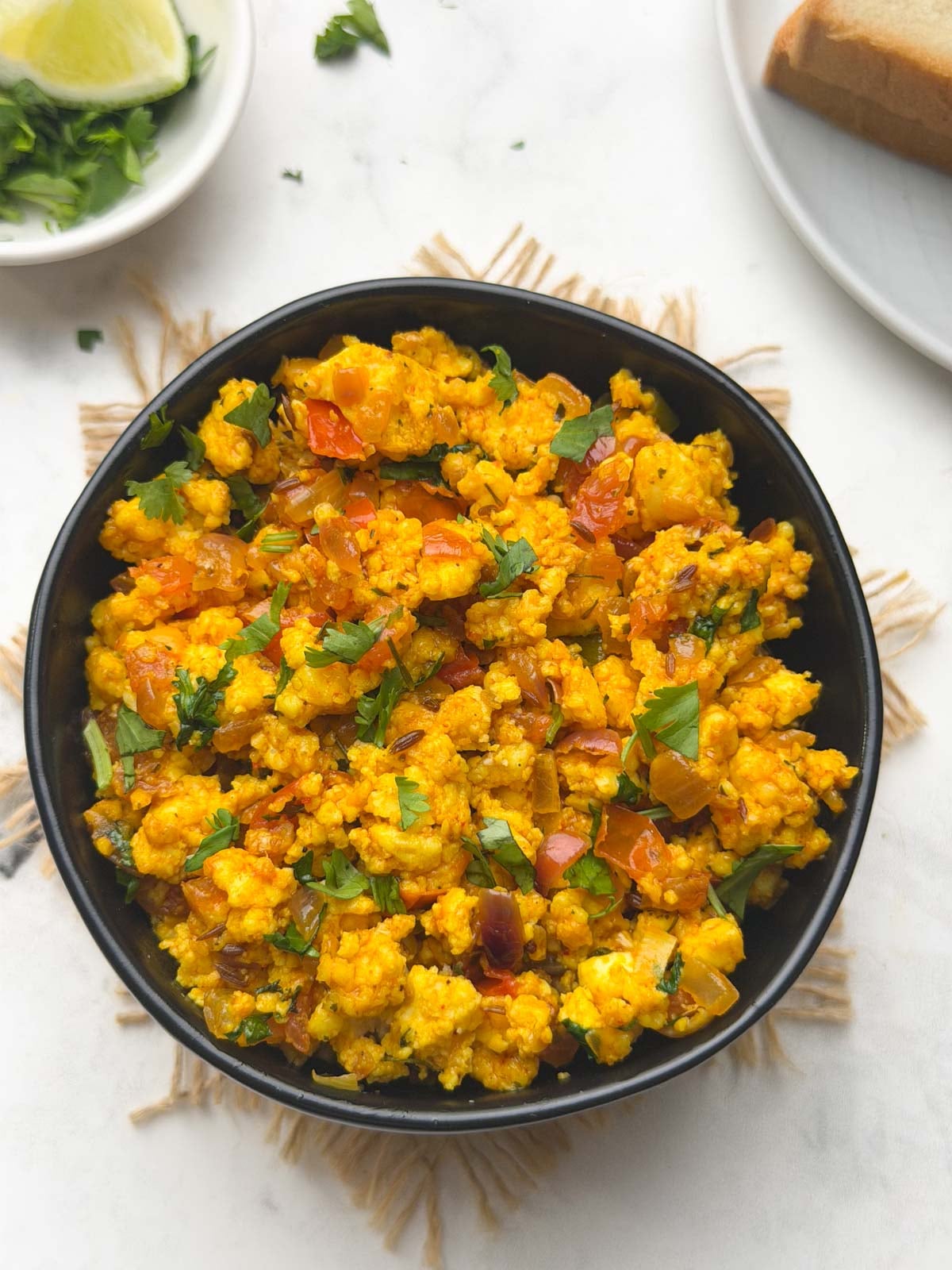 Paneer bhurji served in a black bowl with white bread and coriander leaves for garnish served on the side.