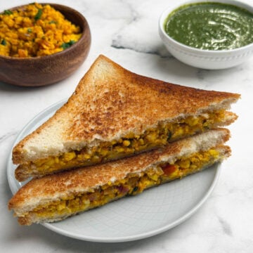 Two paneer bhurji sandwich stacked on a plate with green chutney and paneer bhurji on the side.