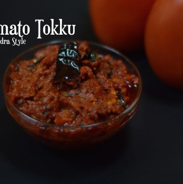 Tomato Thokku Andra Style served in a bowl with two raw tomato on the side