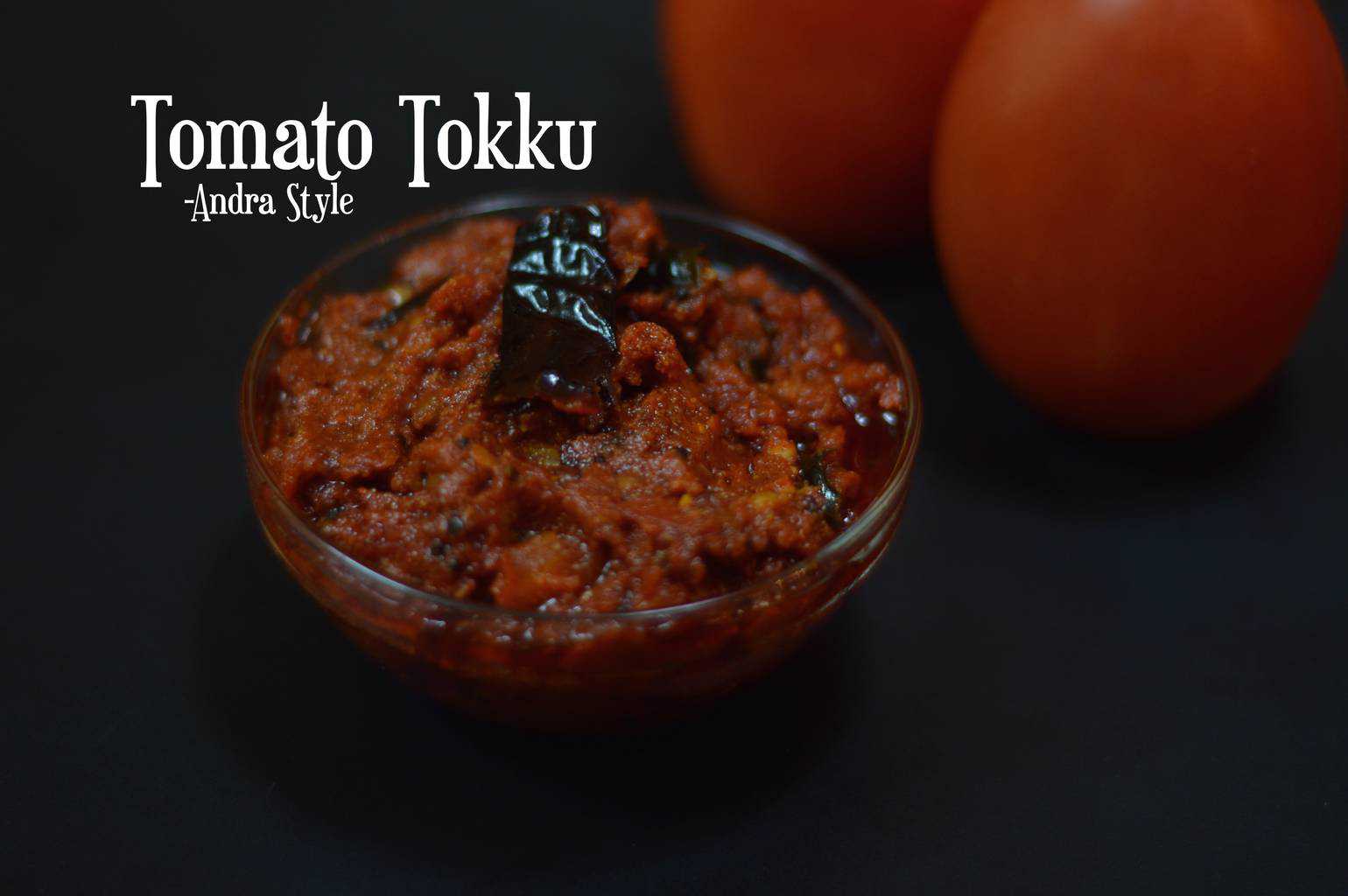 Tomato Thokku Andra Style served in a bowl with two raw tomato on the side