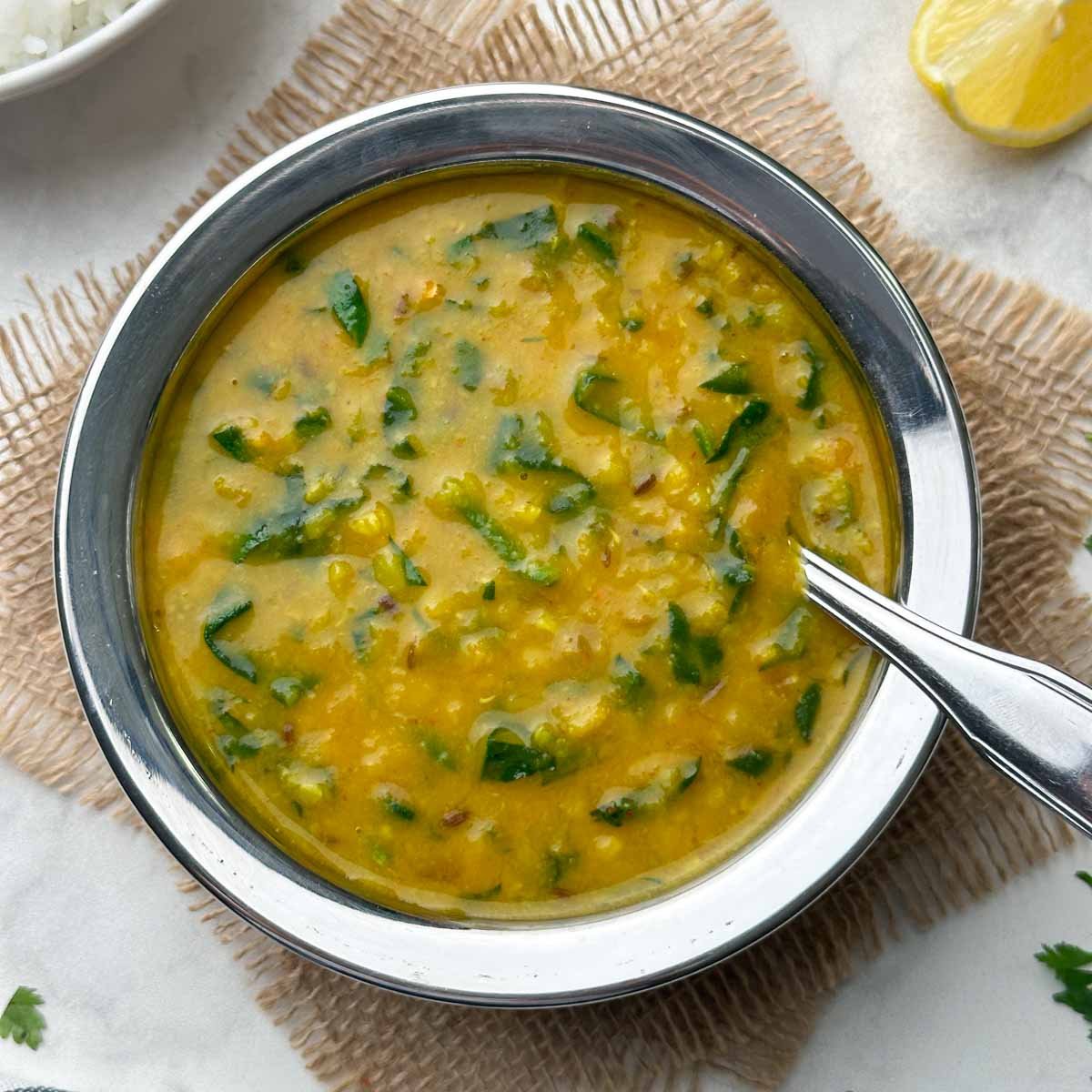 dal palak recipe served in a kadai with a spoon and rice on the side