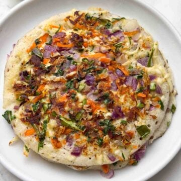 Paneer vegetable uttapams stacked on a white plate with coriander coconut chutney on the side.