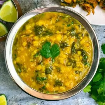 Spinach Dal served in a steel bowl with cilantro and lemon wedges on side