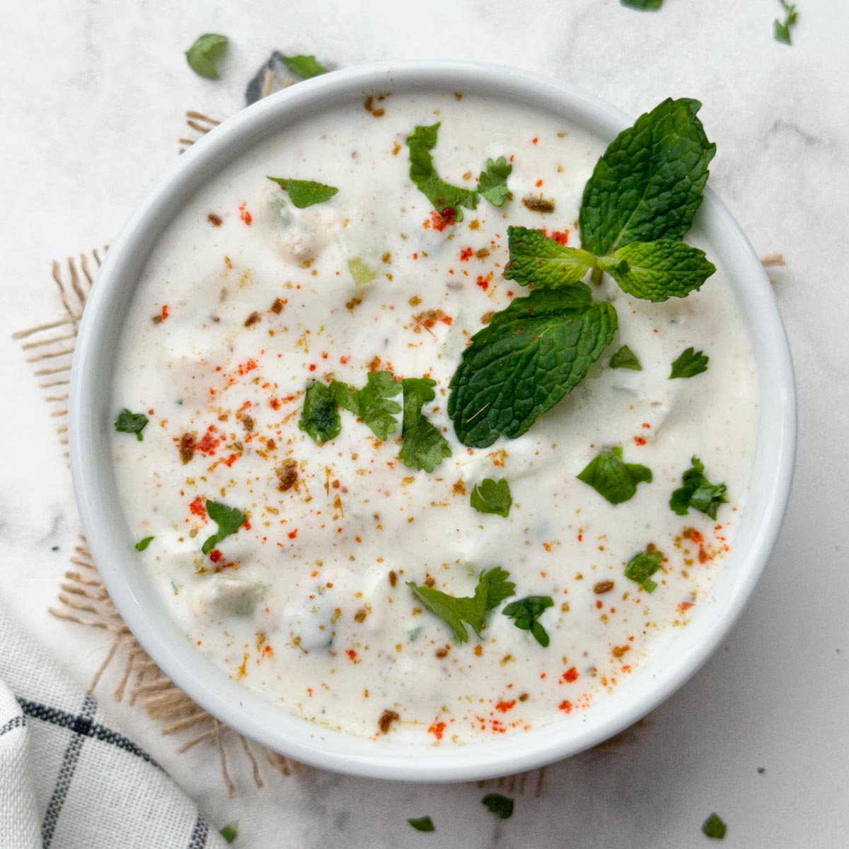 cucumber raita served in a bowl garnished with coriander and mint leaves