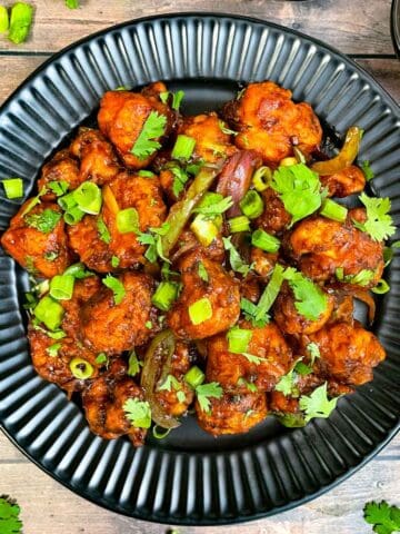 cauliflower manchurian served on a plate garnished with green onions and coriander leaves