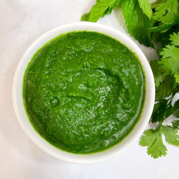 green chutney served in a bowl with mint and coriander leaves on the side