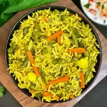 Vegetabilsk pulao serveret i en sort skål og tomatløg raita på siden