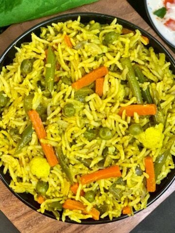 vegetable pulao served in a black bowl and tomato onion raita on side