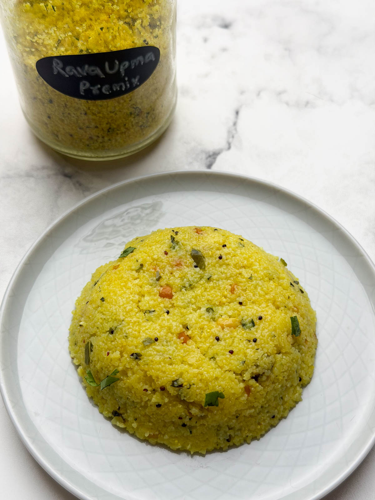 Cooked Rava upma on a plate with rava upma premix in a glass mason jar behind.