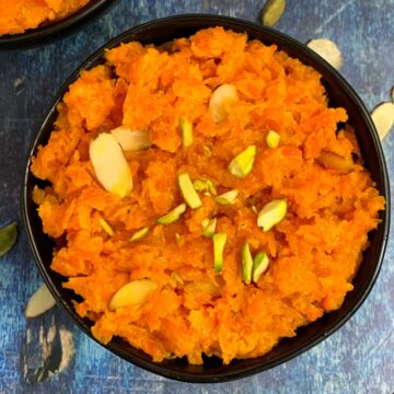 Carrot Halwa served in a black bowl garnished with slivered almonds and pistachios