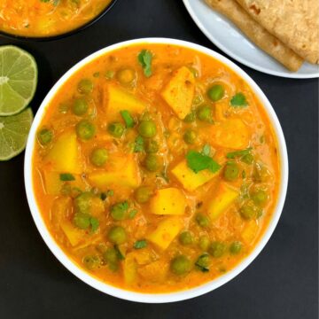potato peas curry served in a bowl garnished with cilantro with chapati and lemon wedge on the side