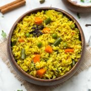 Tamil Nadu style seeraga samba rice veg biryani in a wooden bowl with raita and whole spices in the side