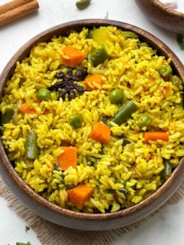 Tamil Nadu style seeraga samba rice veg biryani in a wooden bowl with raita and whole spices in the side