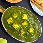 Palak Paneer served in a steel bowl with chapati and lemon wedges on side