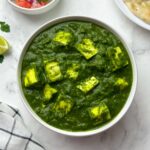 palak paneer served in a white bowl with salad and garlic naan on the side