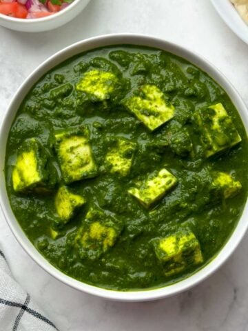 palak paneer served in a white bowl with salad and garlic naan on the side