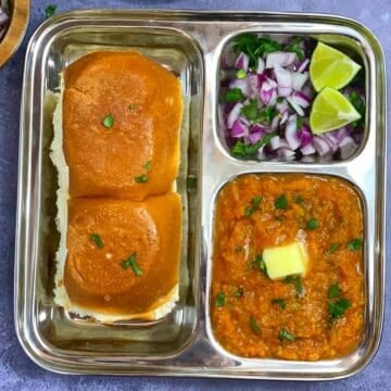 Pav Bhaji served in a steel plate with buttered pav and onion on the side