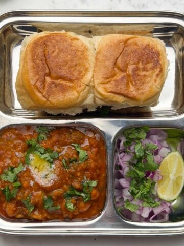 Pav bhaji served in a bento steel plate with onion, coriander and lime wedge.