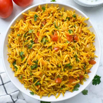 instant pot tomato rice pulao served in a white bowl with whole tomatoes on the side