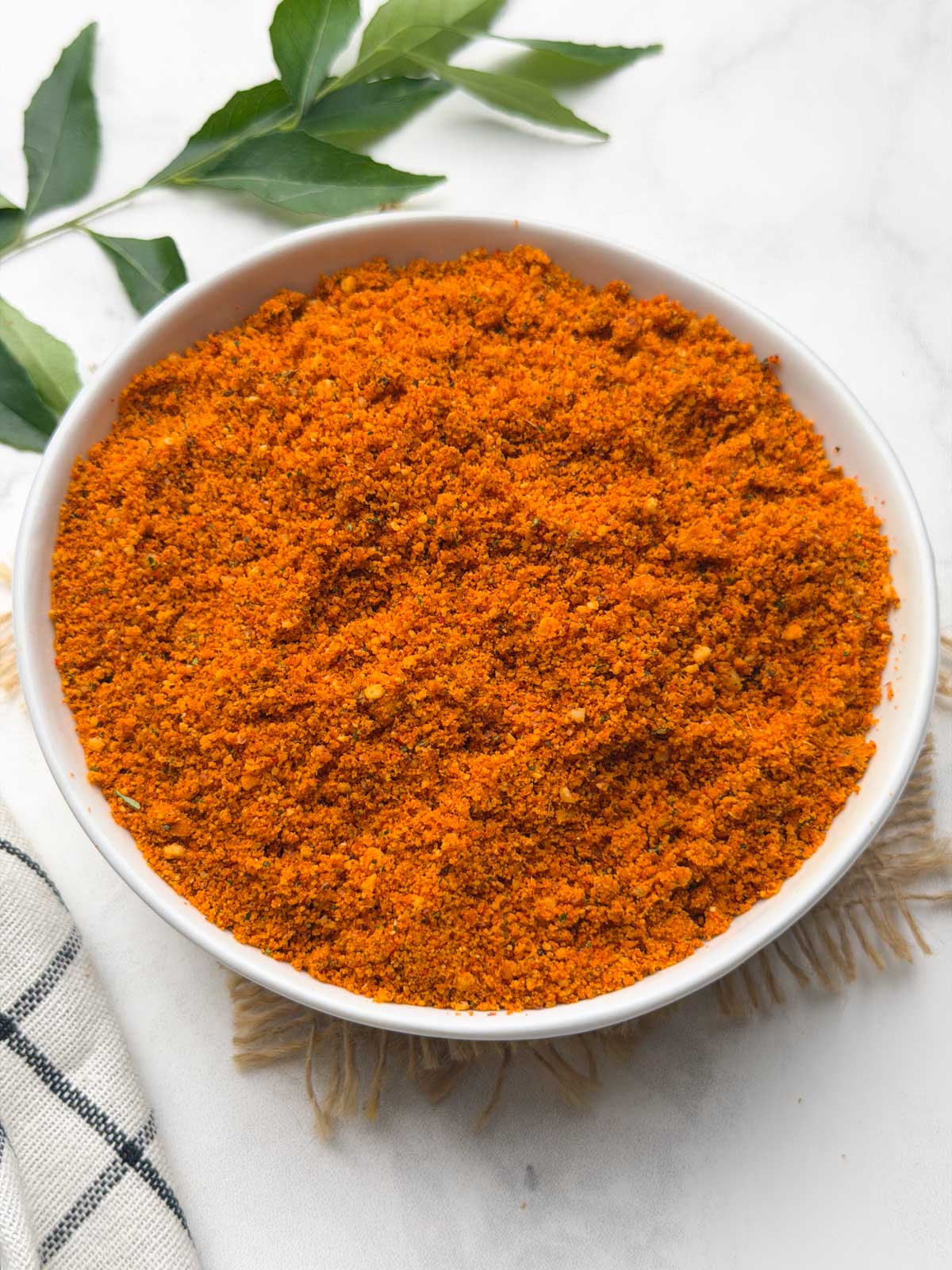 Peanut Chutney powder served in a small bowl with curry leaves on the side for decoration.