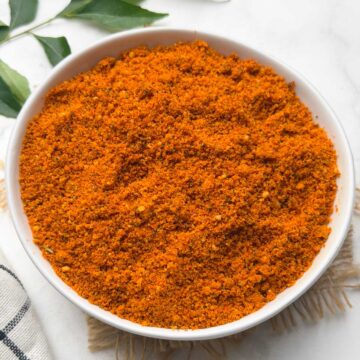 Peanut Chutney powder served in a small bowl with curry leaves on the side for decoration.
