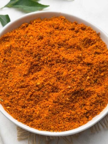 Peanut Chutney powder served in a small bowl with curry leaves on the side for decoration.