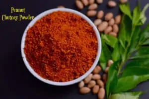 Peanut Chutney Powder (shenga chutney pudi) served in a white bowl with raw peanuts and curry leaves on the side