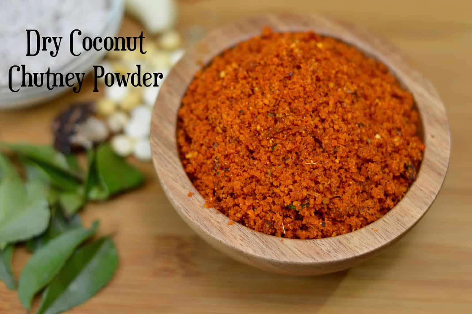 dry coconut chutney powder served in a wooden bowl with curry leaves on the side