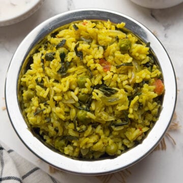Methi rice bhath served in steel bowl with raita and cucumber on the side.