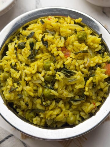 Methi rice bhath served in steel bowl with raita and cucumber on the side.