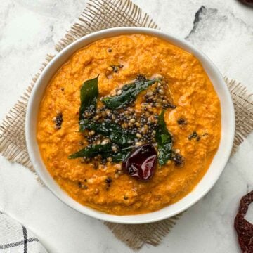 red coconut chutney served in a white bowl with tempering on the top