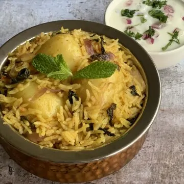Potato Biryani served in a handi garnished with mint with side of raita